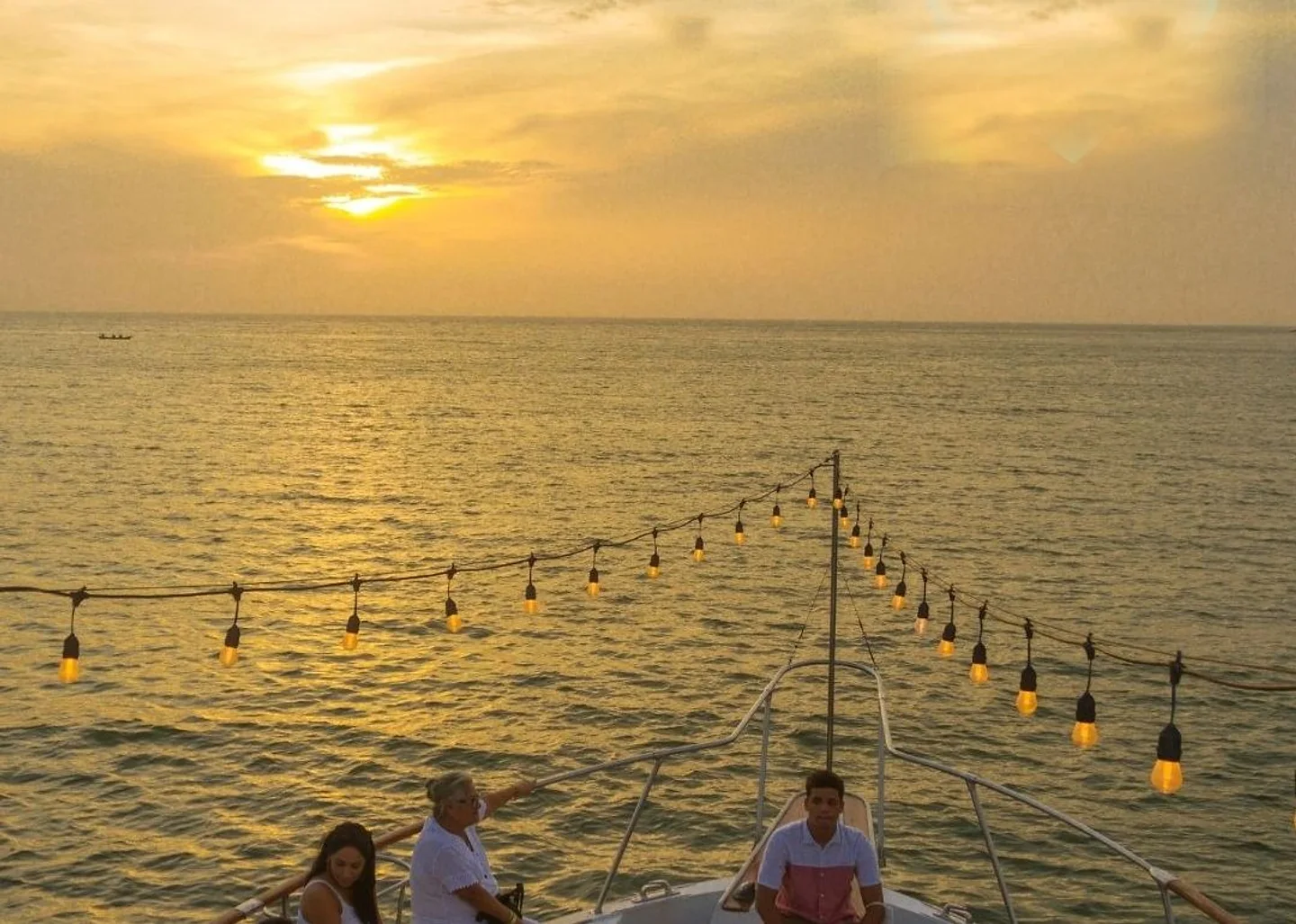 Atardecer sobre la bahía de Cartagena desde la proa de un barco, con guirnalda de luces encendida